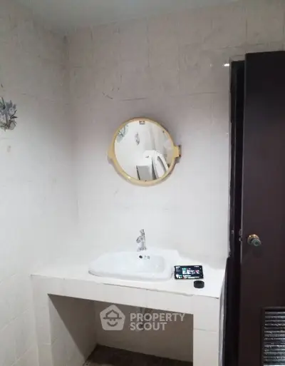Simple bathroom with round mirror and white sink on tiled wall.