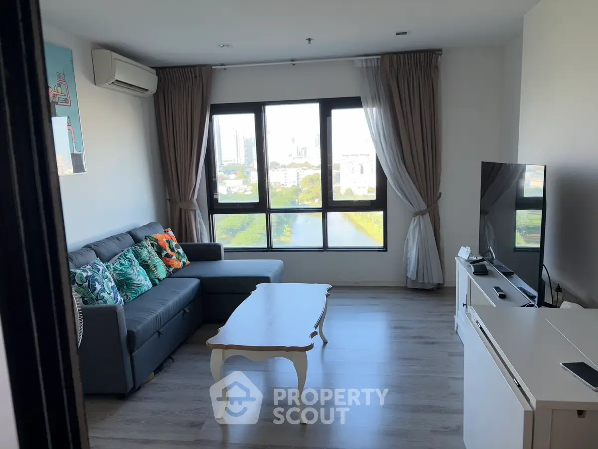 Modern living room with large window and city view, featuring stylish sofa and TV setup.