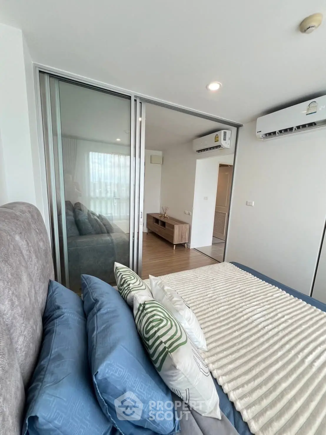 Modern bedroom with sliding glass doors and air conditioning, featuring stylish bedding and contemporary decor.