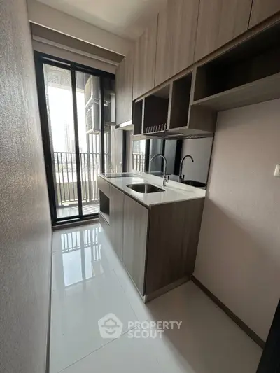 Modern compact kitchen with sleek cabinetry and balcony access in urban apartment.