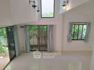 Spacious living room with high ceilings and large windows overlooking a lush garden.