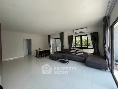 Spacious living room with modern sofa and large windows offering natural light and garden view.