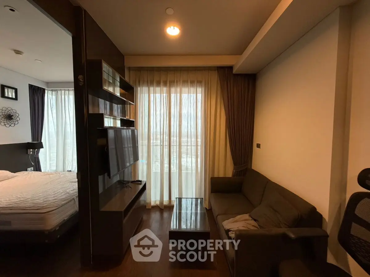 Cozy living room with modern decor and adjacent bedroom, featuring floor-to-ceiling windows.