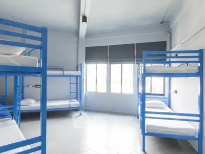 Spacious dormitory room with multiple blue bunk beds and large windows.