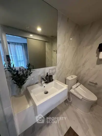 Modern bathroom with sleek fixtures and elegant marble tiles, featuring a stylish sink and toilet.