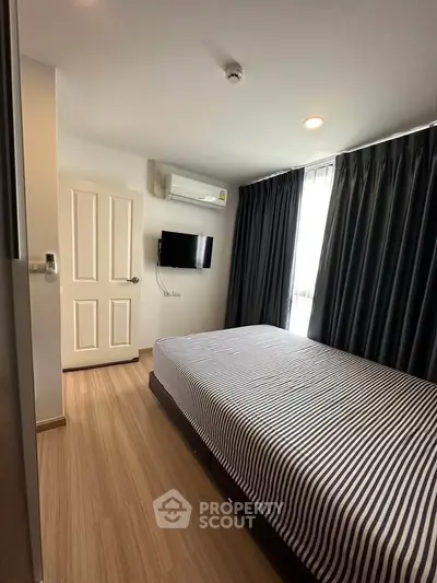 Cozy bedroom with striped bedding and wall-mounted TV, featuring modern decor and natural light.