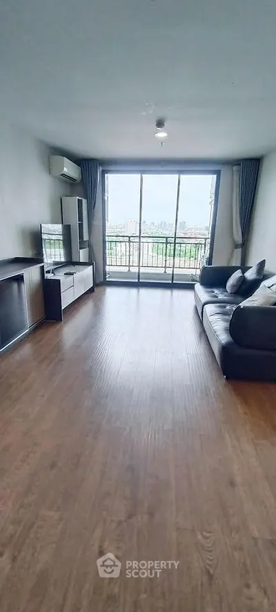 Spacious living room with large windows and city view, featuring modern furniture and wooden flooring.