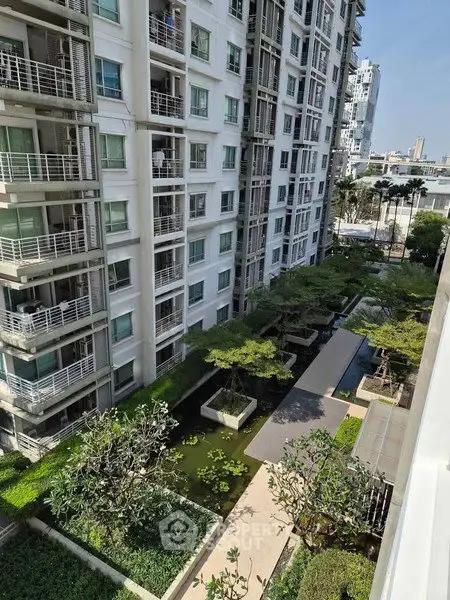 Modern apartment building with lush garden and water features in urban setting.