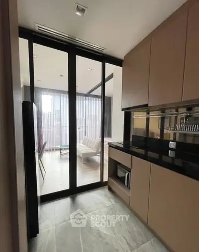 Modern kitchen with closed layout and sleek cabinetry leading to a stylish living room.
