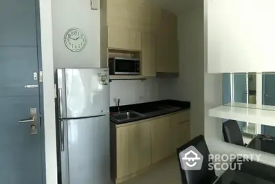 Modern compact kitchen with fridge, microwave, and sleek cabinetry in a stylish apartment.