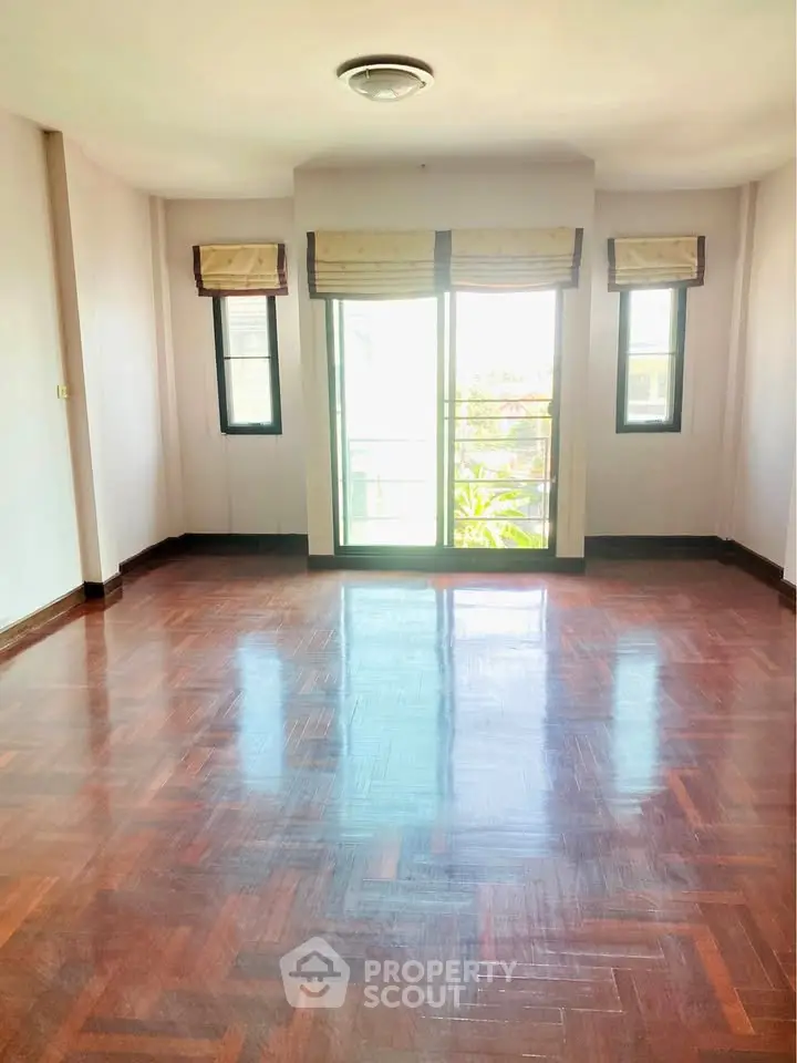 Spacious sunlit room with polished wooden floors and large windows.