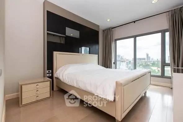 Modern bedroom with large window and city view, featuring elegant decor and natural light.