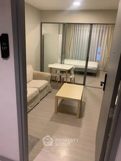Modern studio apartment with open layout, featuring cozy living area and bedroom separated by glass doors.