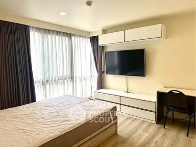 Modern bedroom with large window, sleek furniture, and mounted TV in a stylish apartment.