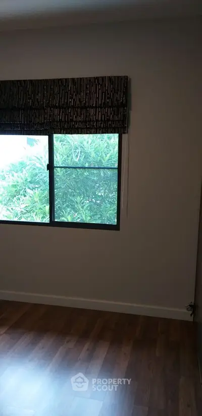 Serene living space with polished wooden flooring and a large window offering a lush green view, perfect for a tranquil lifestyle.