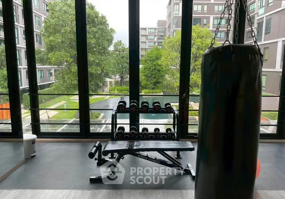 Modern gym with punching bag and weights overlooking lush garden in luxury apartment complex.