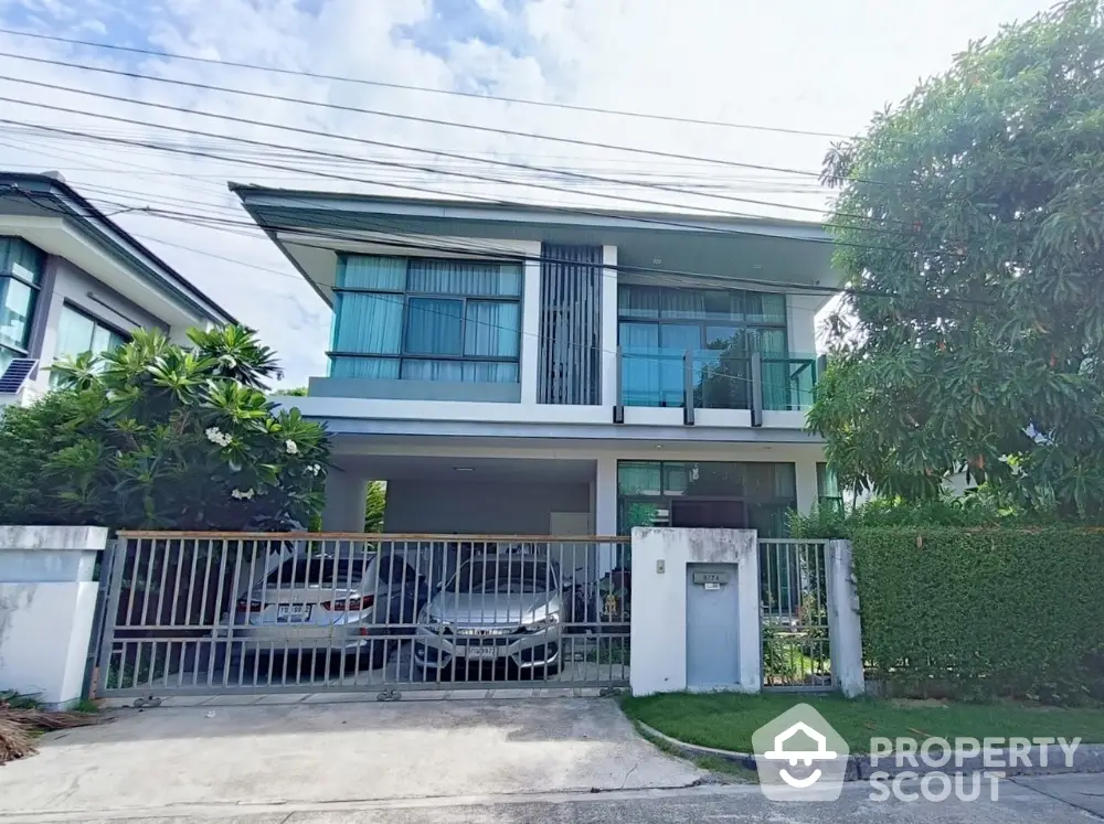 Modern two-story house with large windows and gated driveway in suburban neighborhood.