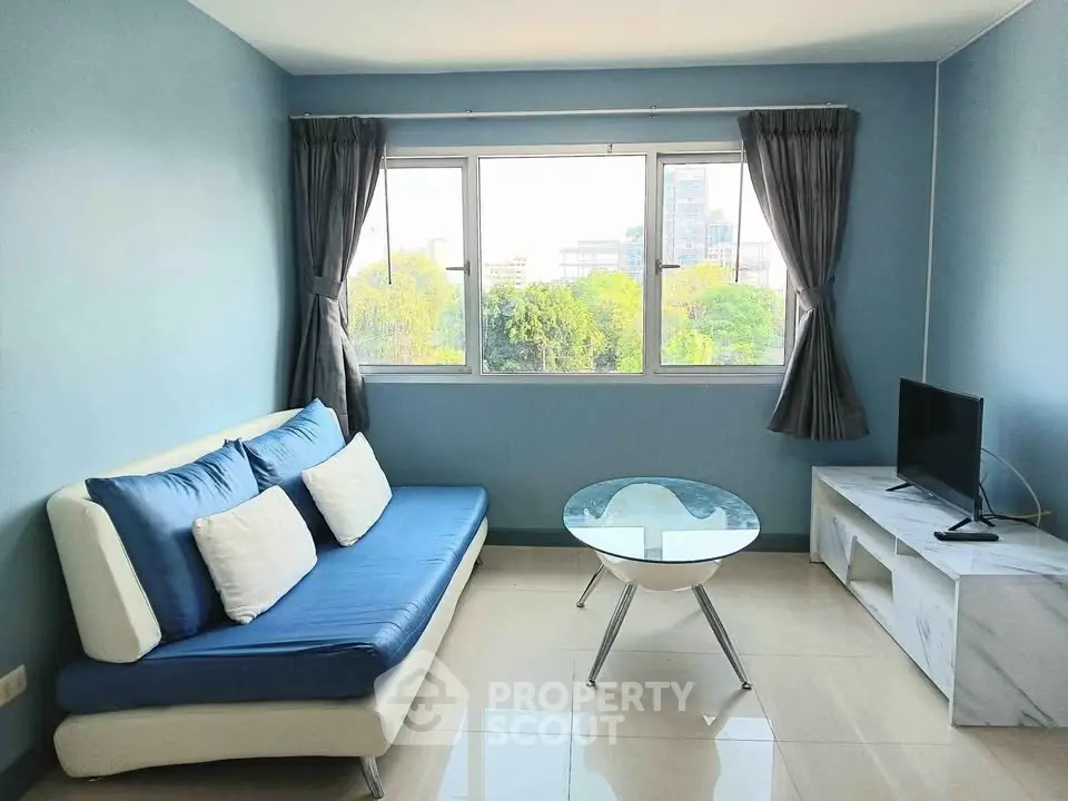 Bright living room with modern sofa, glass coffee table, and large window with city view.