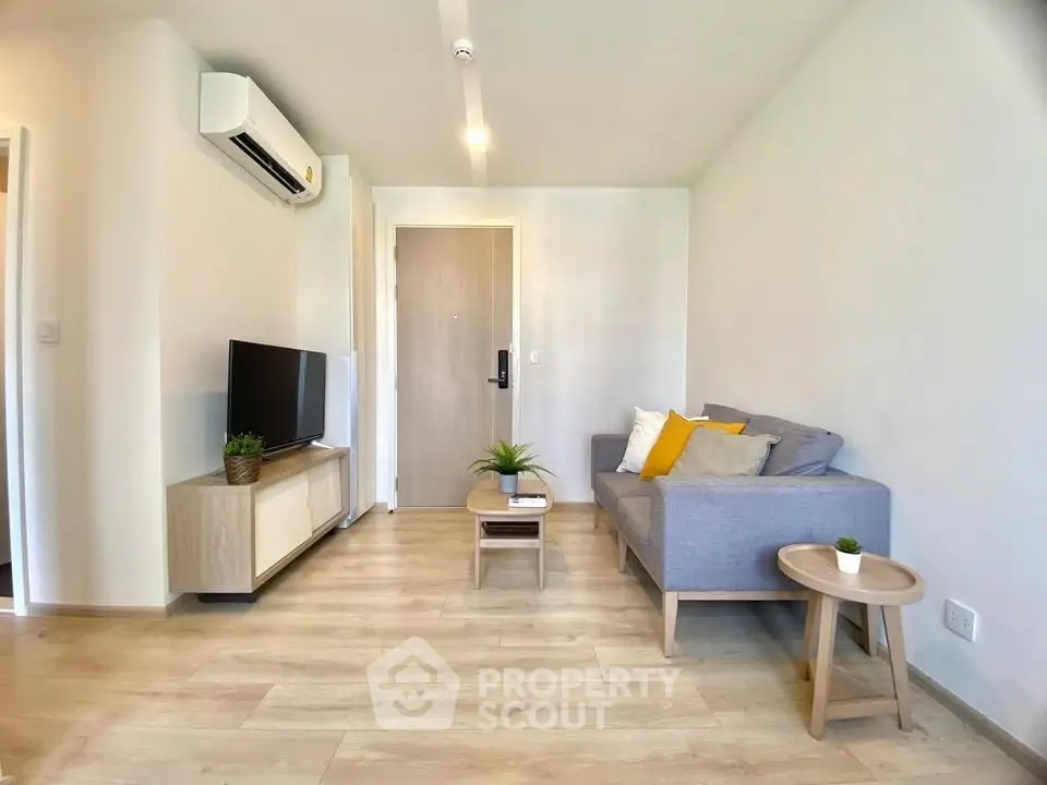 Modern living room with sleek wooden flooring, cozy gray sofa, and stylish TV unit.
