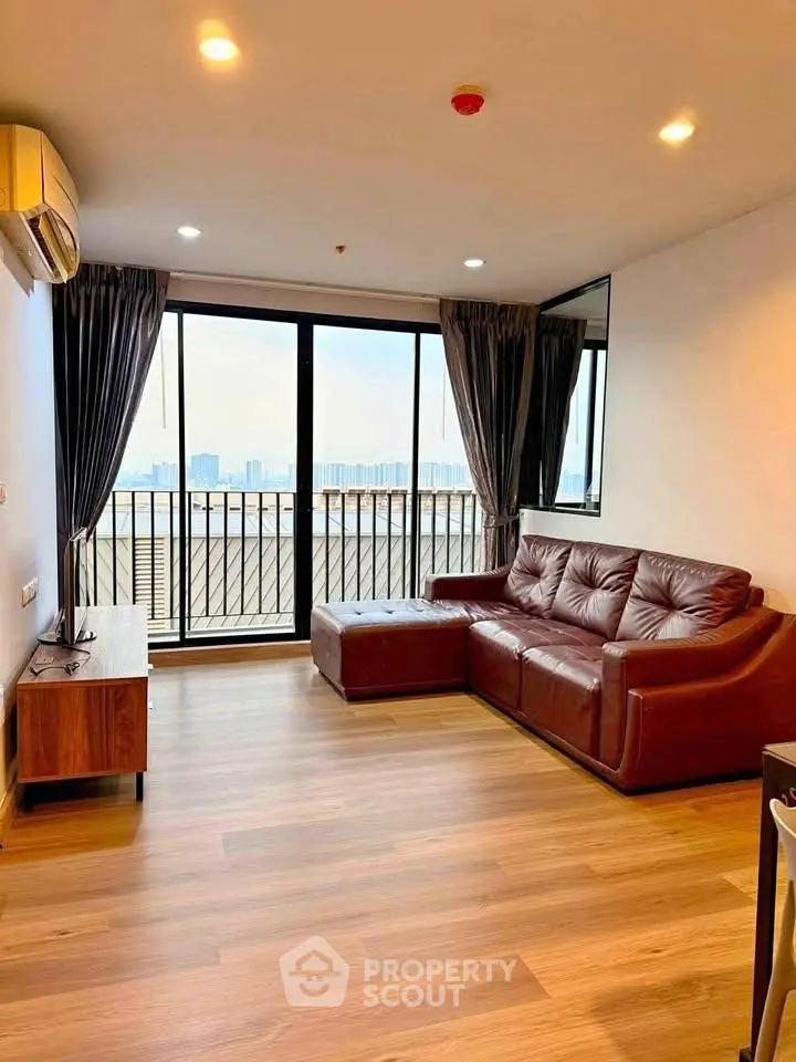 Spacious living room with leather sofa and city view balcony in modern apartment.