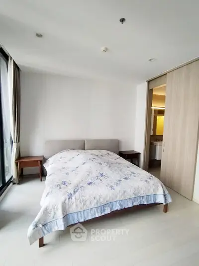 Spacious bedroom with large window and ensuite bathroom in modern apartment.
