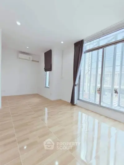 Spacious sunlit room with large windows and polished wooden floors, perfect for modern living.