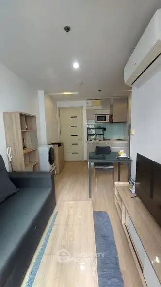 Modern living room with open kitchen, featuring sleek furniture and appliances.