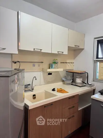Compact kitchen with modern cabinets and appliances, featuring a sleek countertop and stainless steel fridge.