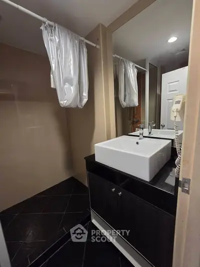 Modern bathroom with sleek black vanity and square sink, featuring a spacious shower area and elegant design.