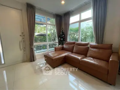 Spacious living room with leather sofa and large windows overlooking garden.
