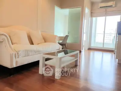 Spacious living room with elegant sofa and glass coffee table, featuring wooden flooring and natural light.