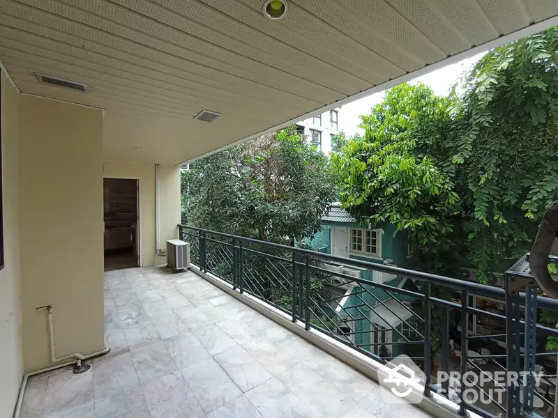 Spacious balcony with elegant tile flooring and lush greenery view, perfect for outdoor relaxation and entertaining in a serene urban setting.