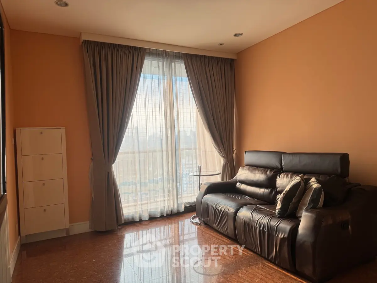 Spacious living room with elegant curtains and leather sofa, featuring a warm ambiance and natural light.