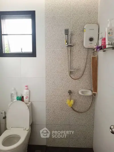 Modern bathroom with shower and toilet, featuring tiled walls and natural light.