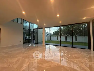 Spacious modern living room with large windows and marble flooring, offering a serene garden view.