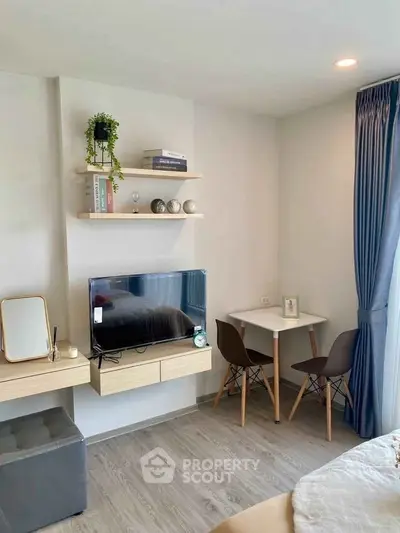 Cozy modern bedroom with TV, shelves, and small dining area near window.