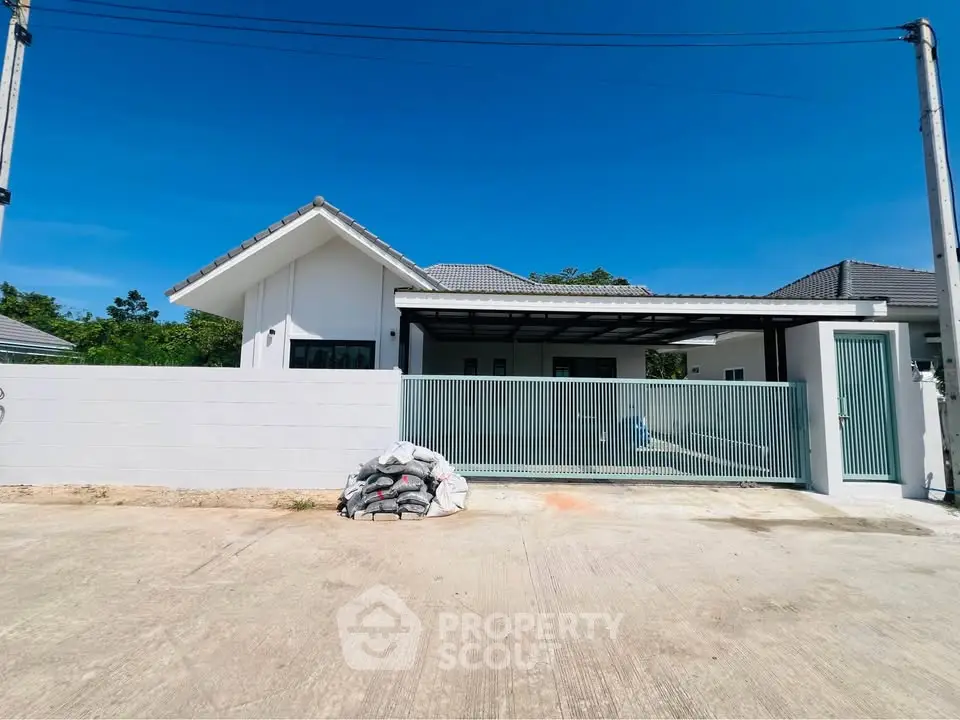 Modern single-story house with gated entrance and spacious driveway under clear blue sky.