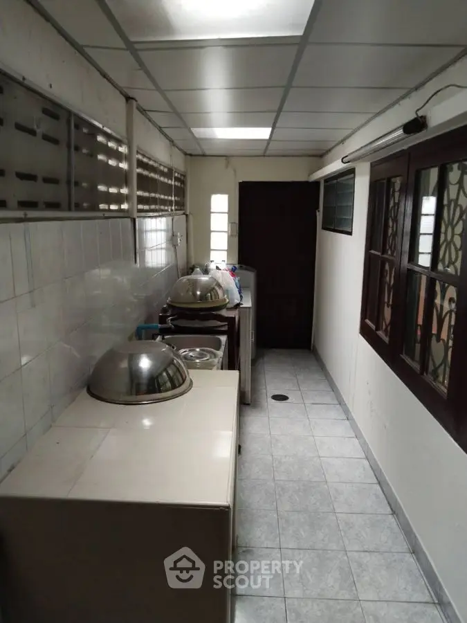 Narrow kitchen space with tiled floor and ceiling lights, featuring closed layout and basic appliances.