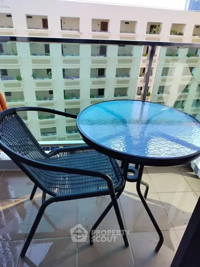 Charming balcony with modern glass table and chair overlooking urban building view.