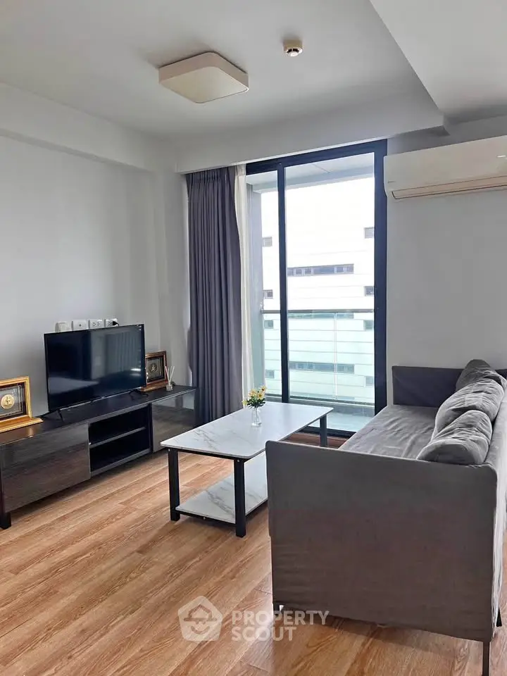 Modern living room with sleek furniture and large window offering natural light and city view.