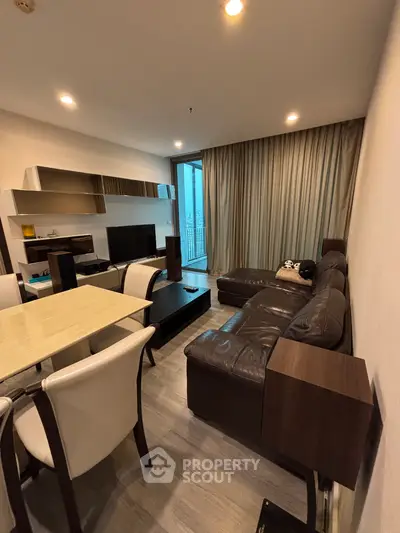 Modern living room with leather sofa and dining area, featuring floor-to-ceiling windows and stylish decor.