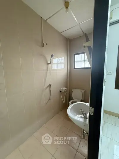 Simple bathroom with shower, toilet, and sink in a tiled setting.