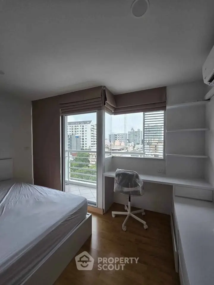 Modern bedroom with city view, featuring a bed, desk, and balcony access in a high-rise apartment.
