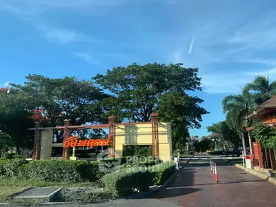Charming residential entrance with lush greenery and clear blue sky.