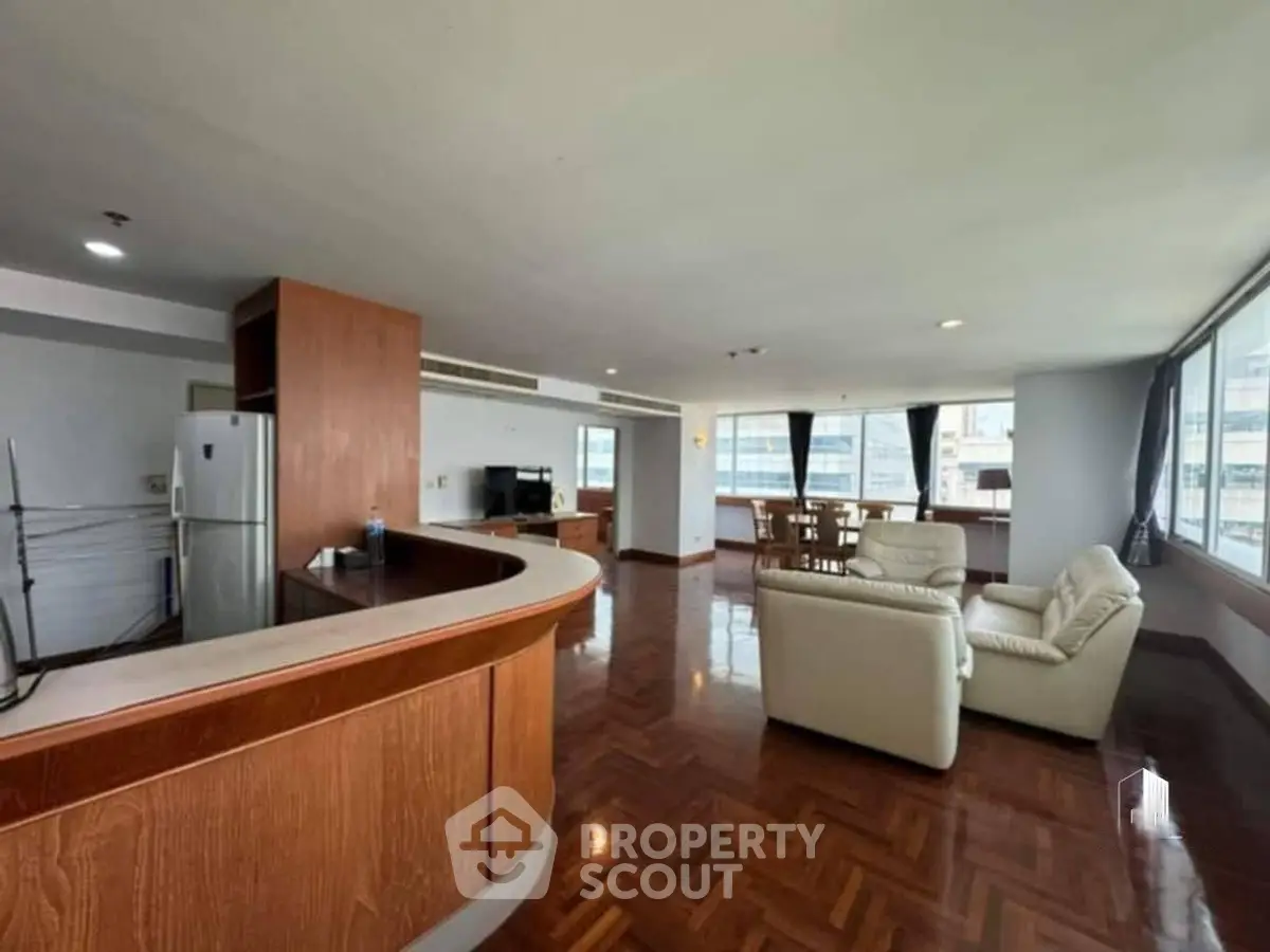 Spacious open-plan living room with modern kitchen and dining area, featuring large windows and wooden flooring.