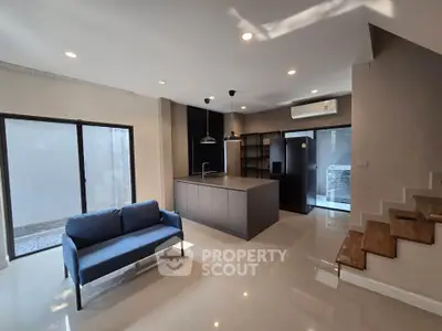 Modern open-plan living room with sleek kitchen and stylish staircase in a contemporary home.