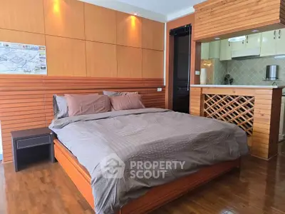 Spacious bedroom with modern wooden accents and open kitchen layout in stylish apartment.