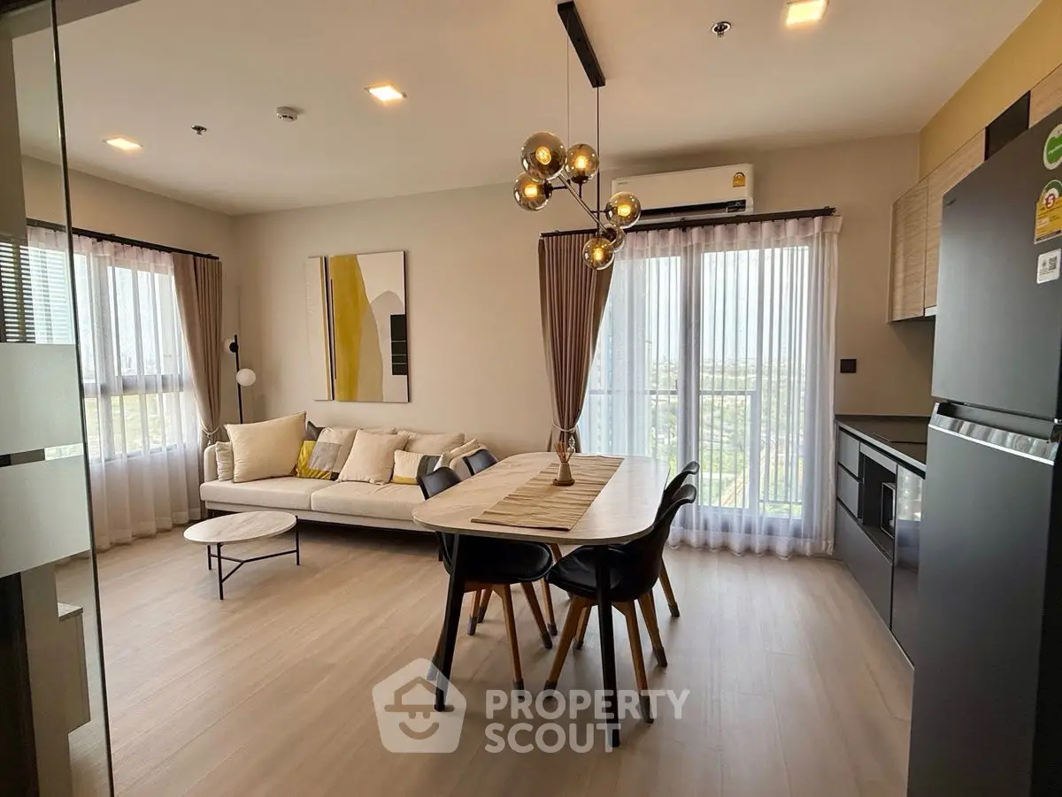 Modern living room with stylish decor and open kitchen layout, featuring elegant lighting and large windows.