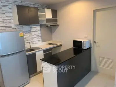Modern kitchen with sleek cabinetry and appliances, featuring a stylish black countertop and stainless steel fridge.