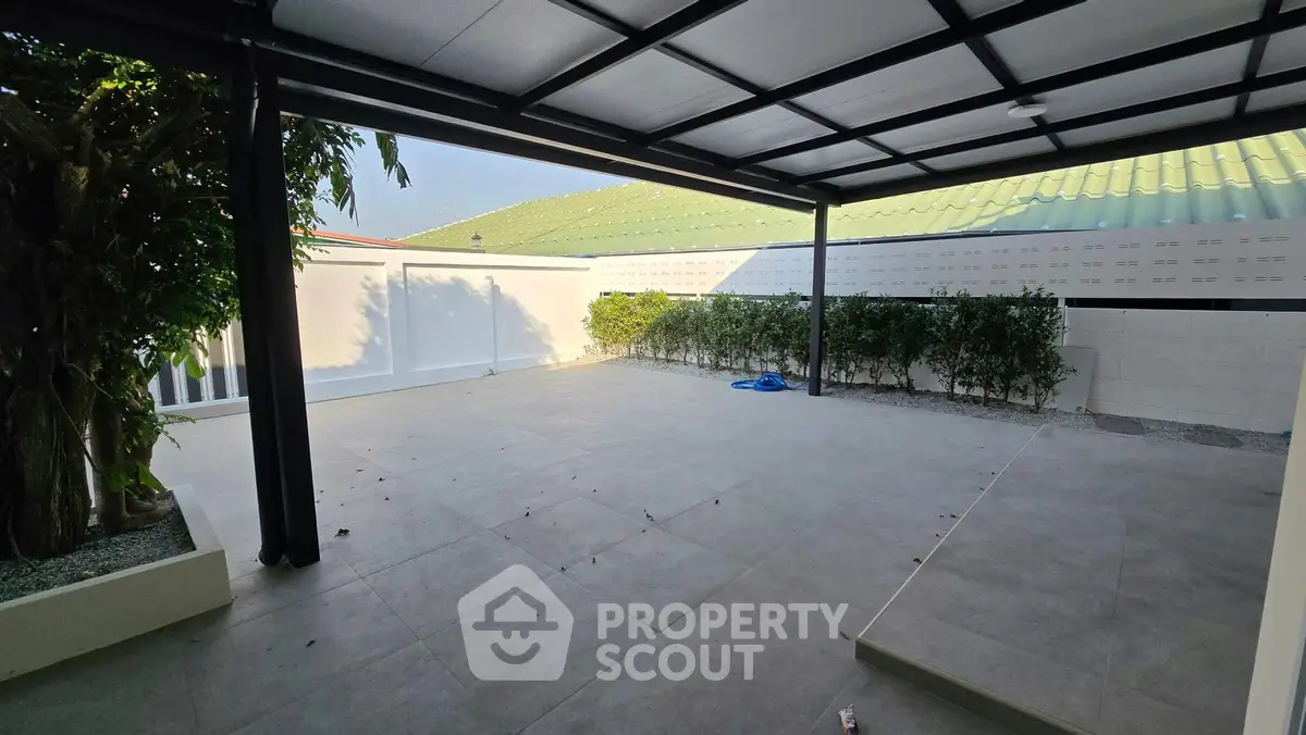 Spacious covered patio with tiled flooring and lush greenery, perfect for outdoor relaxation.